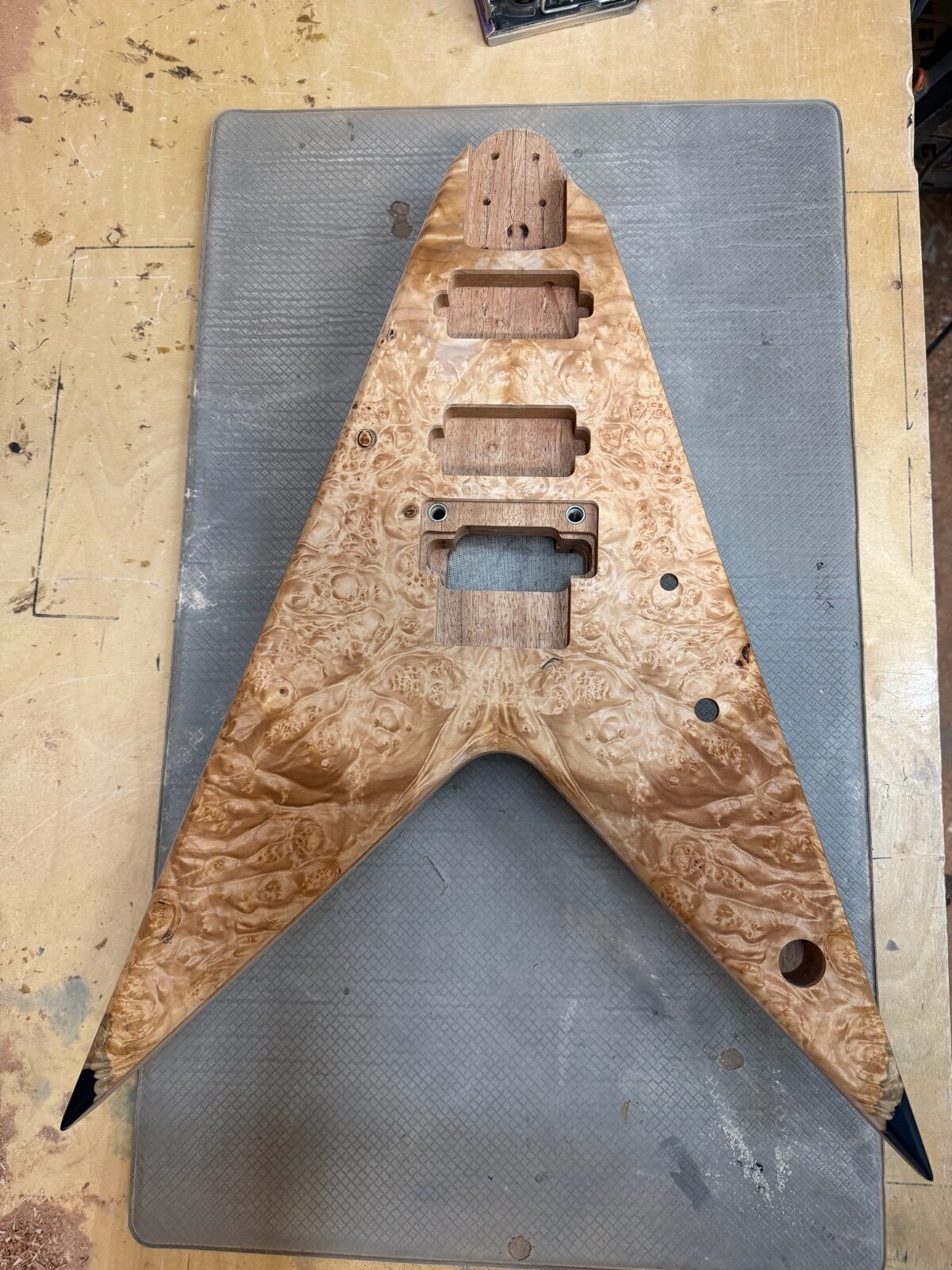 Raw burl-top V-style guitar body with routed pickup cavities, in progress